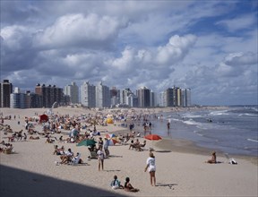 URUGUAY, Punta del Este, "Busy, sandy beach with people sunbathing, playing ball games and in surf.