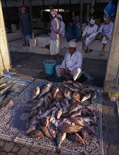 UAE, Oman, Muscat, Mutrah fish market.  Vendor sitting behind display of whole fish scattered with