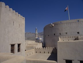 UAE, Oman, Nizwa, Minaret and blue and gold domed roof of mosque seen from fort walls with barren
