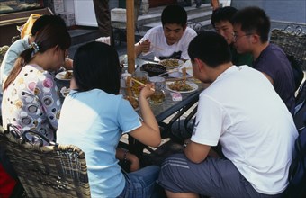 CHINA, Beijing, "Wangfujing shopping street.  Group of young people using chopsticks to eat meal,