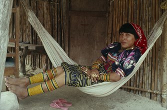 PANAMA, San Blas Islands, Kuna Indians, Young Kuna mother rests in hammock outside home  wearing