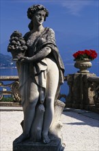 ITALY, Lombardy, Lake Como, Villa Balbianello.  Statue of woman holding basket of fruit with red