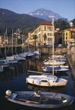 ITALY, Lombardy, Lake Como, Menaggio.  Harbour with moored boats and waterside buildings with tree