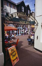 ENGLAND, East Sussex, Hastings, Westhill Arcade. Gate leading to shops with people sitting at cafe