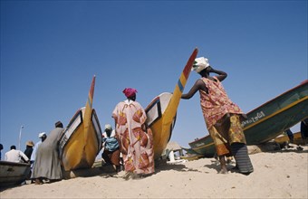 SENEGAL, Soumbedioune, Women wearing brightly coloured traditionally patterned clothing on beach