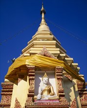 THAILAND, North, Chiang Mai, Seated Buddha statue in decorated recess below gold chedi wrapped in