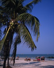 THAILAND, Hua Hin, Western tourists on Hua Hin beach with distant boats on the water and coconut