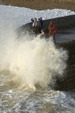 ENGLAND, East Sussex, Brighton, Waves crashing onto beach and groyne with people getting wet.