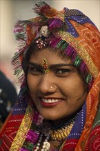 INDIA, Rajasthan, Alwar, Portrait of a female dancer smiling wearing a multi coloured head dress at