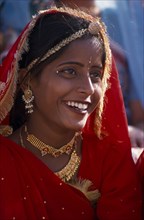 INDIA, Rajasthan, Bikaner, Portrait of a girl dancer smiling wearing red and gold at the Camel