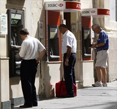 MALTA, Valletta, Three men using separate ATM cash machines on Republic Street