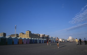 ENGLAND, East Sussex, Brighton, Joggers on Hove Lawns Esplanade by colourful beach huts in late