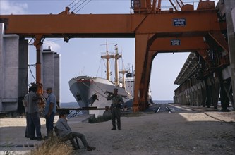 CUBA, Industry, Soldiers in dockyard with container ship moored behind framed by huge steel crane.