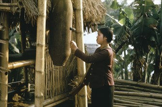 VIETNAM, North Central, War, Young woman using bomb casing as an air raid warning device.
