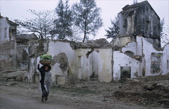 VIETNAM, North, War, Woman carrying basket of vegetables on her head passing ruins of war damaged
