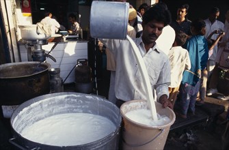 INDIA, Delhi, Street market scene with man pouring milk into bucket.