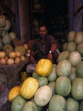 BANGLADESH, Dhaka, Man selling durians and melons in fruit market.