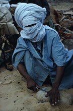 ALGERIA, Sahara Desert, Tuareg, "Tuareg man sharpening tool on rock, wearing blue taguelmoust