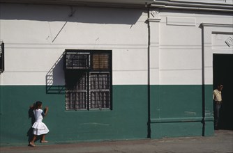 NICARAGUA, Leon, Street scene with little girl in white outside building painted dark green and