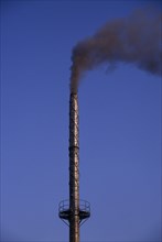INDIA, Madhya Pradesh, Bhopal, Tall factory chimney emitting black smoke against blue sky.
