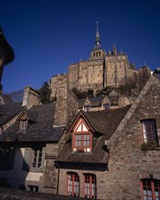 FRANCE, Normandy, Mont-St-Michel, The Abbey on hilltop above tiled rooftops of town houses from the