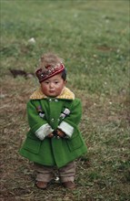 CHINA, Children, Portrait of young Kazakh child wearing green wool coat and embroidered cap.