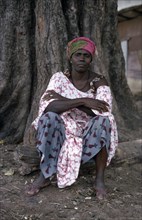 SENEGAL, People, Portrait of woman seated at base of tree trunk wearing fabric of different printed