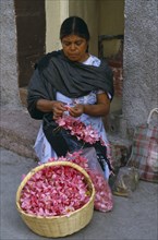 MEXICO, Guerrero, Woman flower seller sitting on step in street threading pink flower heads into
