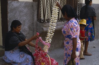 MEXICO, Guerrero, Woman vendor and customer at flower market stall looking at frangipani flower
