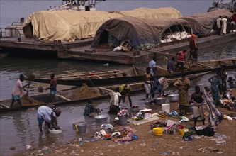 SENEGAL, Niger River, Women washing clothes in river from bank with barges and wooden canoes