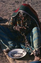 INDIA, Rajasthan, People, Kalbelia gypsy woman in traditional dress stringing beads.