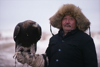 20088819 CHINA Xinjiang Province People Kazakh man wearing thick  fur lined hat and holding eagle on his gloved hand.