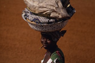 20088675 CENTRAL AFRICAN REPUBLIC  People Woman on her way to market carrying laden bowls on her head and chewing on a teeth cleaning stick.