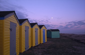 ENGLAND, West Sussex, Littlehampton, Row of  yellow and green beach huts next to promenade seen in