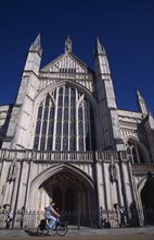 ENGLAND, Hampshire, Winchester, Winchester Cathedral exterior with a man travelling past on a
