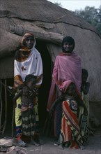 ETHIOPIA, North East, People, Afar women and children standing outside entrance of domed hut behind