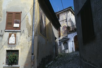 ITALY, Lombardy, Arcumeggia, Narrow cobbled street with fresco decoration and plaster relief of the