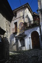 ITALY, Lombardy, Arcumeggia, Narrow cobbled street with fresco decoration on exterior wall of