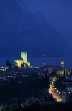 ITALY, Veneto, Lake Garda , Malcesine.  Tiled rooftops of town and castle illuminated at night with