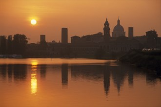 ITALY, Lombardy, Mantua, City view at sunset reflected in water.