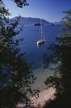 ITALY, Lake Maggiore, "Yacht anchored on lake framed by trees in foreground.  Stretch of pebble