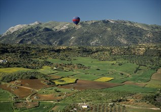 SPAIN, Andalucia, Malaga , A hot air balloon flying over green valley with patchwork fields towards