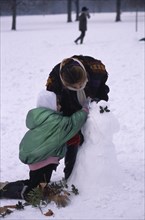 ENGLAND, London, Hyde Park, Two girls building snowman decorated with holly leaves.