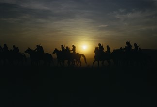 SAUDI ARABIA, Animals, Hunting party on horseback silhouetted against sunset sky.