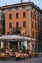 ITALY, Lombardy, Salo, People sitting beneath white awning at outside tables of cafe in piazza of