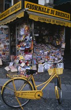 ITALY, Lombardy, Brescia, Piazza della Loggia.  Newspaper stand with yellow painted bicycle