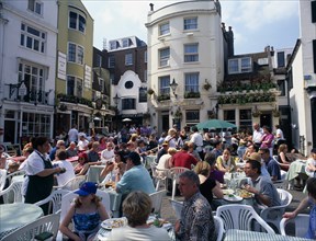 ENGLAND, East Sussex, Brighton, The North Lanes. East Street. People eating and drinking at tables