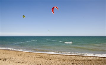 ENGLAND, West Sussex, Lancing, Kite Surfers on sea next to shingle beach in the summer with blue