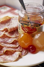 ITALY, Lombardy, Cremona, "Open jar of Mostarda di Cremona and salami.  Type of fruit preserve