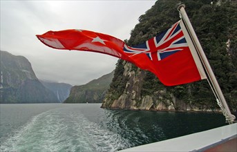 NEW ZEALAND, SOUTH ISLAND, "MILFORD SOUND,", "SOUTHLAND, A NEW ZEALND ENSIGN FLAG WAVES ON THE REAR